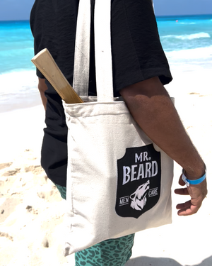 Person holding a tote bag with 'Mr. Beard' logo on a beach