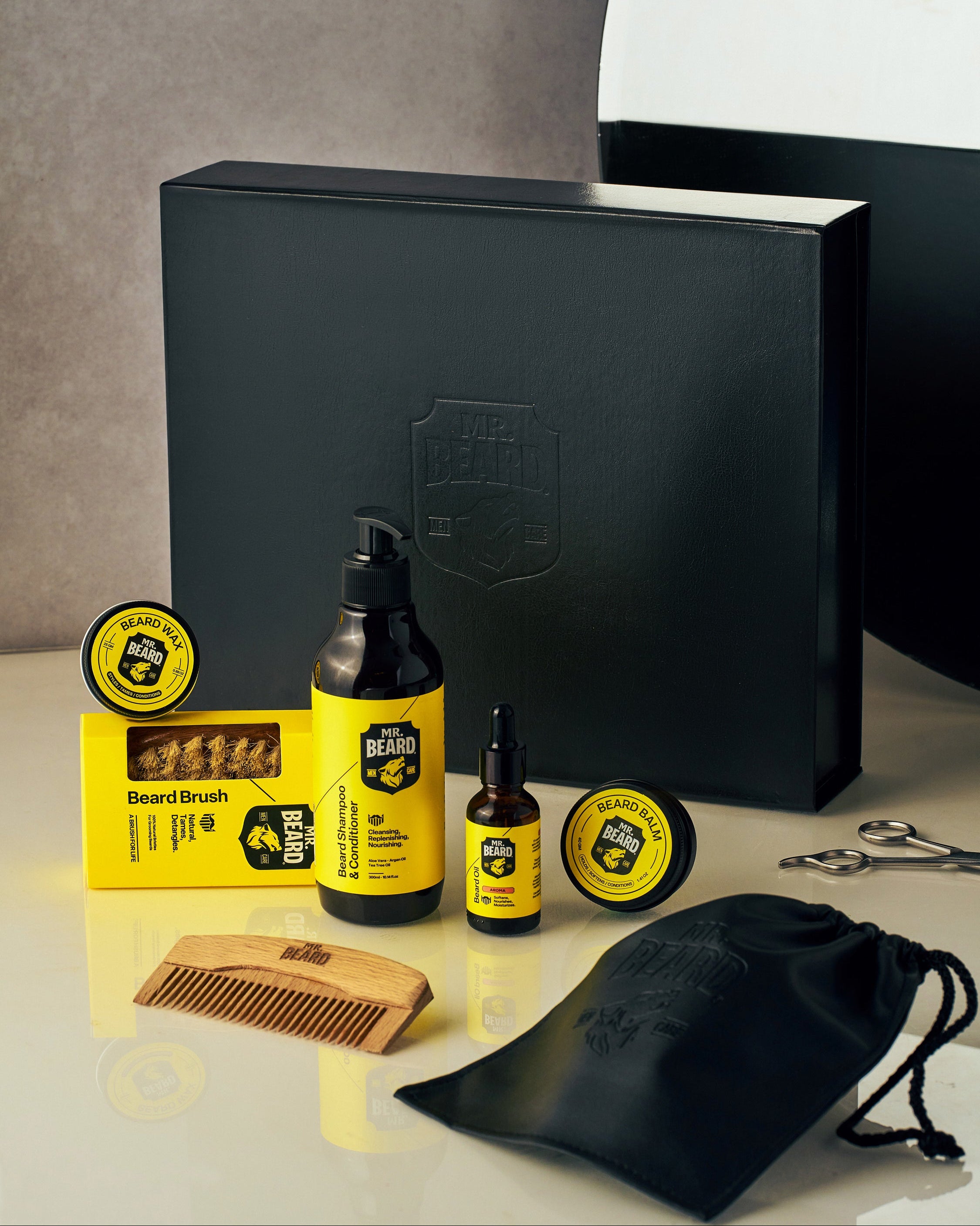 Beard grooming products including a bottle, brush, and other items displayed in front of a black box.