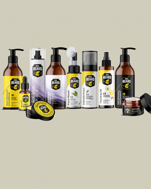 A lineup of beard care products from The Beard Brand, including beard oil, beard balm, beard wash, and beard treatment, arranged on a solid light beige background.