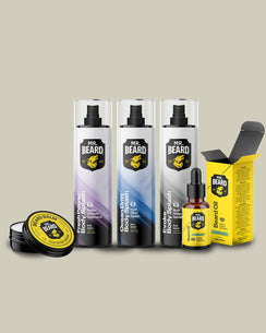A 4-piece beard grooming kit by Beard Bros. on a solid beige background, including three body sprays, a beard oil bottle with its yellow box, and a beard balm tin.